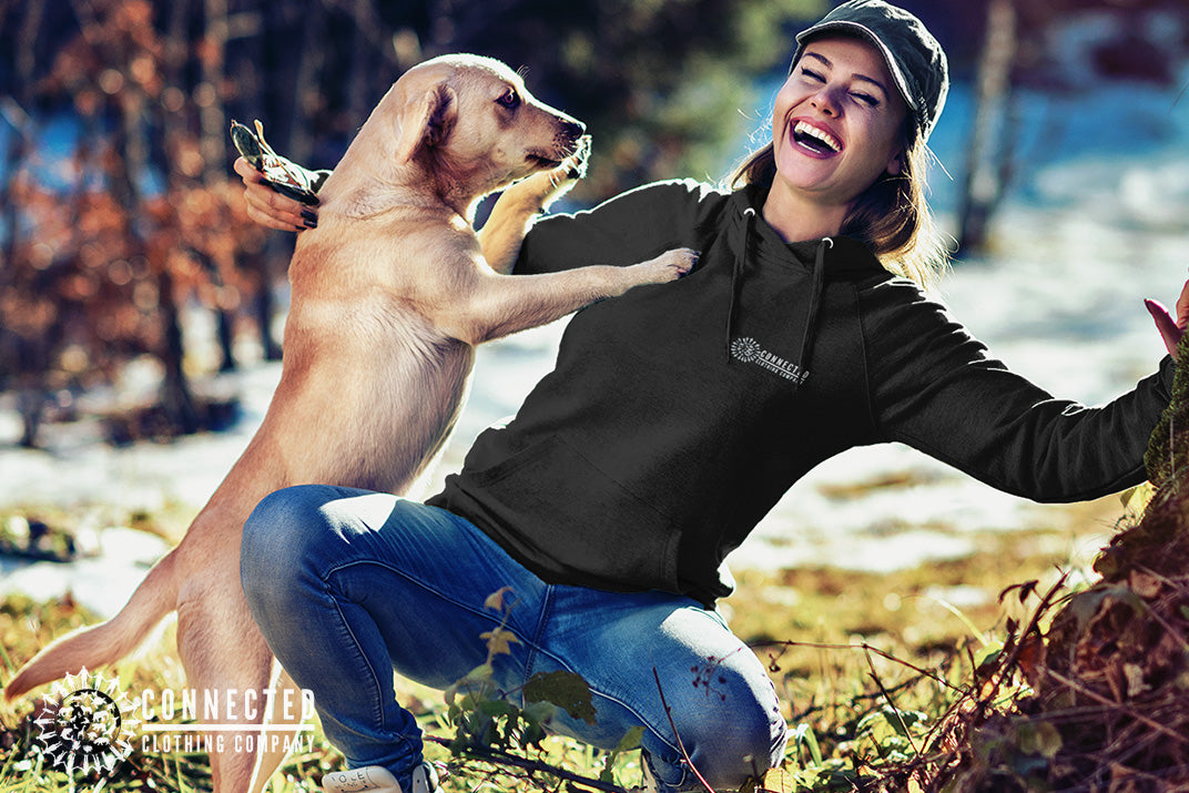 Model wearing Black Show Humanity Unisex Hoodie while smiling and playing with a rescue dog - iguanadelabarra - Ethically and Sustainably Made - 10% donated to the Society for the Prevention of Cruelty to Animals